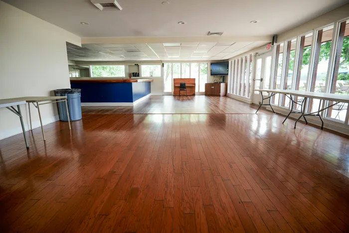 Spacious community room featuring elegant hardwood floors, large windows with abundant natural light, and versatile seating arrangements.