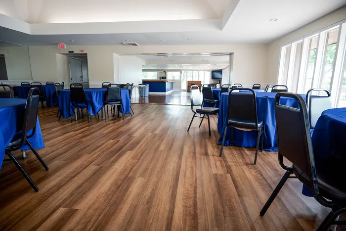 Elegant event space featuring polished wood flooring, bright windows, and tables with vibrant blue tablecloths, perfect for gatherings.