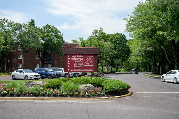 Inviting entrance to Salem Harbour Apartments featuring a welcoming sign surrounded by lush greenery and modern parked cars.