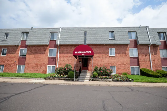 Charming red-brick apartment building with beautifully manicured gardens and a welcoming leasing office entrance.