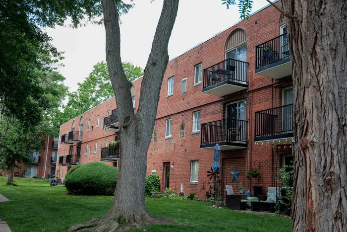 Charming brick apartment building with private balconies, nestled among lush trees and greenery for a serene urban living experience.