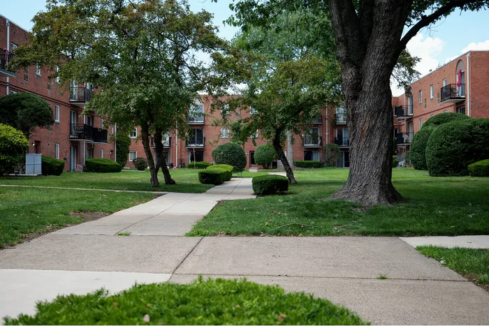 Charming red-brick apartment complex with lush greenery and inviting walking paths, ideal for peaceful living.