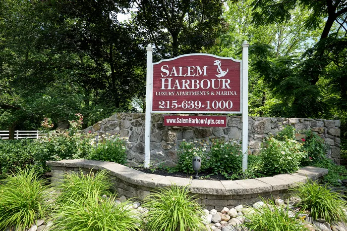 Inviting entrance sign for Salem Harbour Luxury Apartments & Marina surrounded by lush greenery and colorful flowers.