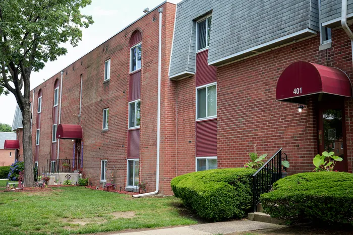 Charming brick apartment building with red accents, lush landscaping, and inviting entrances for modern living.