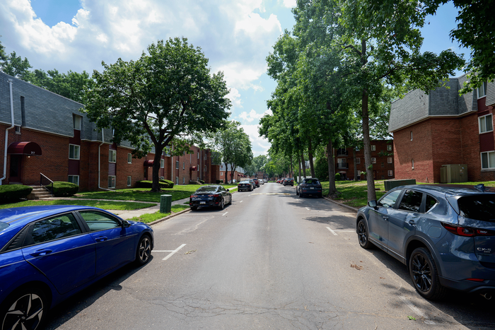 Charming street view with brick apartment buildings framed by lush trees and parked cars, showcasing a serene residential area.