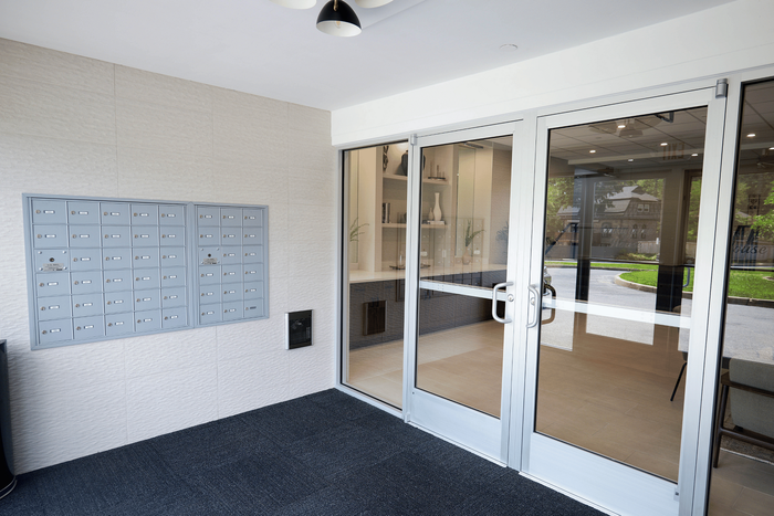 Inviting apartment lobby entrance with sleek glass doors, modern mailboxes, and a view of landscaped greenery outside.