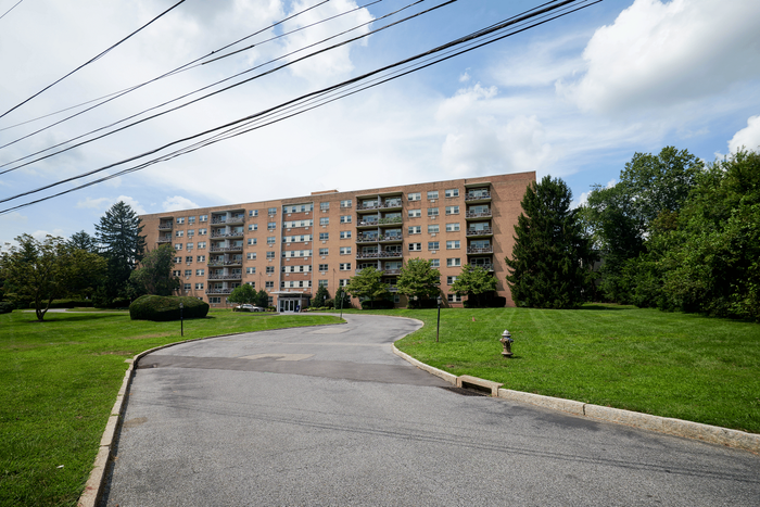 Inviting multi-story apartment complex with lush green lawns and a welcoming entrance, set against a picturesque sky.