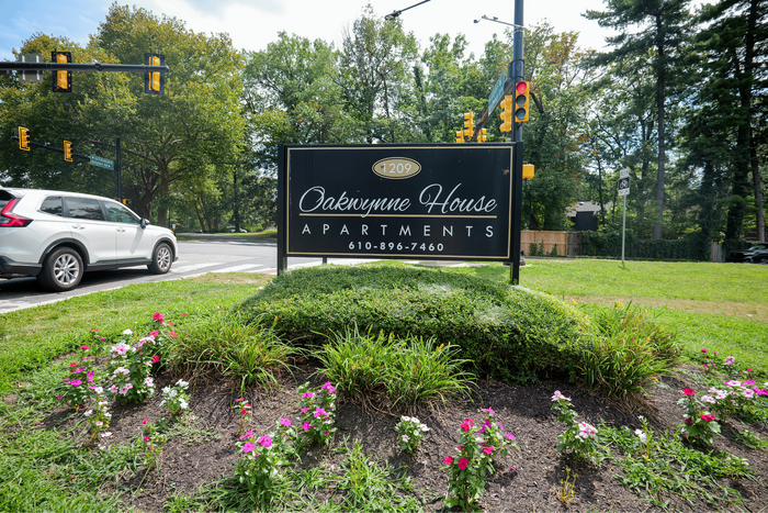 Welcoming sign for Oakwynne House Apartments surrounded by vibrant flower beds and lush greenery.