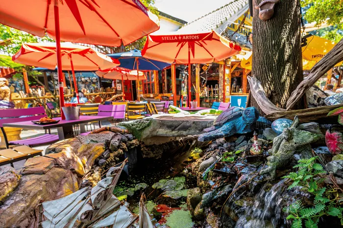 Vibrant outdoor cafe scene featuring colorful umbrellas, eclectic seating, and whimsical sculptures, perfect for a lively gathering.