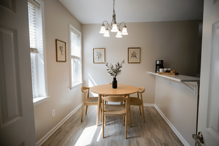 Charming dining area with natural light, featuring a round wooden table, elegant chairs, and tasteful decor.