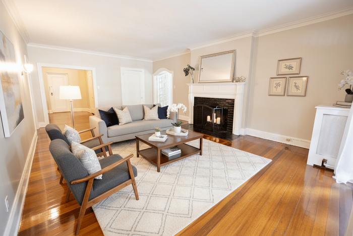 Inviting living room with elegant hardwood floors, cozy gray sofa, chic modern armchairs, and a classic fireplace adorned with decor.