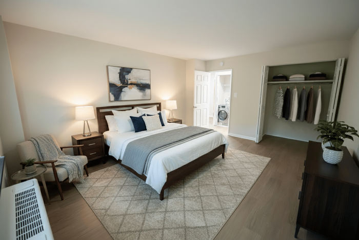 Elegant master bedroom with modern decor, featuring a cozy armchair, stylish artwork, and a spacious open closet.