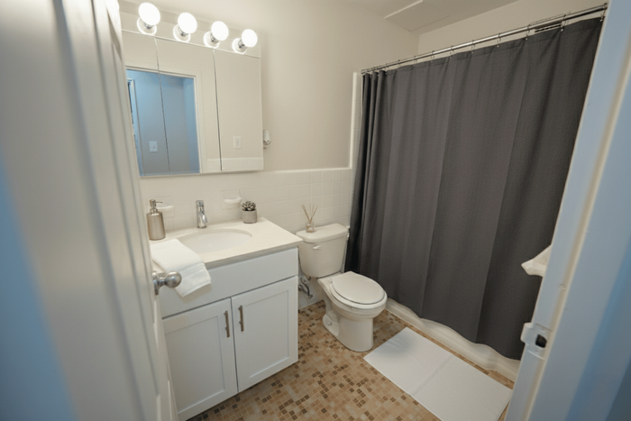 Modern bathroom with elegant white cabinetry, large mirror, and sleek tile flooring, offering a serene and stylish ambiance.