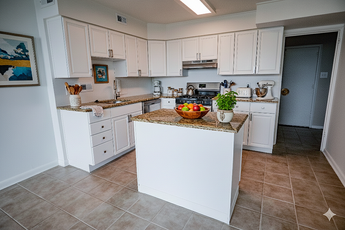 Bright and modern kitchen featuring elegant white cabinetry, a sleek granite countertop island with fresh fruit, and stylish decor accents.