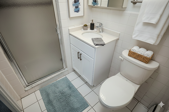 Modern bathroom with sleek glass-enclosed shower, elegant white vanity, and plush blue bath mat for a luxurious touch.