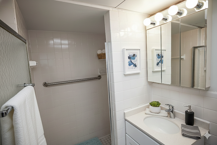 Bright and modern bathroom with elegant lighting, sleek vanity, and stylish decor including framed art and a potted plant.