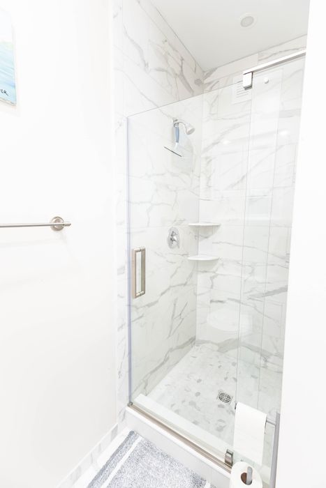 Luxurious marble-tiled shower with glass doors and modern fixtures in a bright, elegant bathroom.