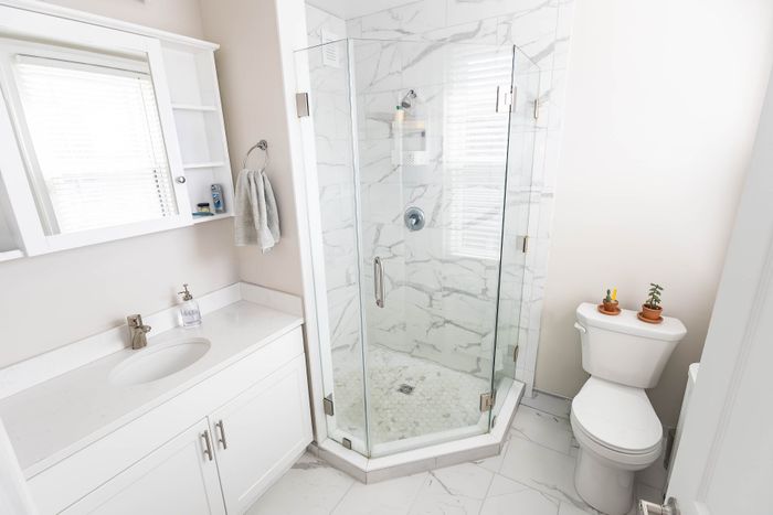 Modern bathroom featuring a sleek glass shower, elegant white vanity, and stylish marble tiles.