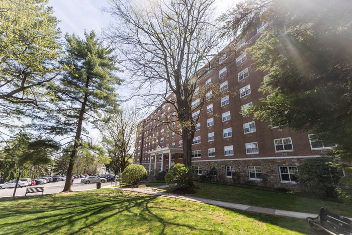 Charming brick apartment complex nestled among lush trees, offering serene outdoor spaces and ample parking.