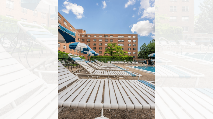 Inviting outdoor pool area with striped lounge chairs and umbrellas, set against a charming brick apartment building under a bright blue sky.