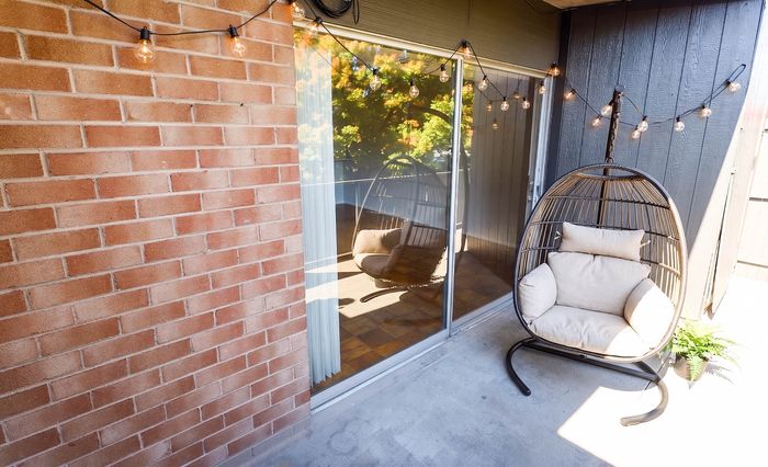 Charming balcony with cozy hanging chair, string lights, and a scenic view through sliding glass doors.