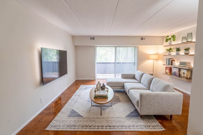 Elegant living room with a modern L-shaped sofa, sleek wall-mounted TV, and stylish decor including plants and books on floating shelves.