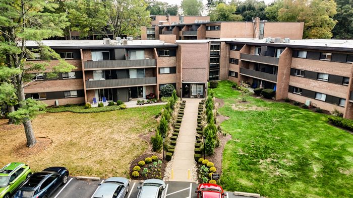 Scenic view of a modern apartment complex with lush green landscaping, well-maintained pathways, and ample parking spaces, ideal for comfortable living.