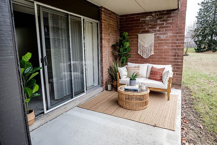 Cozy outdoor patio featuring a stylish wicker loveseat, vibrant green plants, and elegant macram&eacute; wall decor, perfect for relaxation.