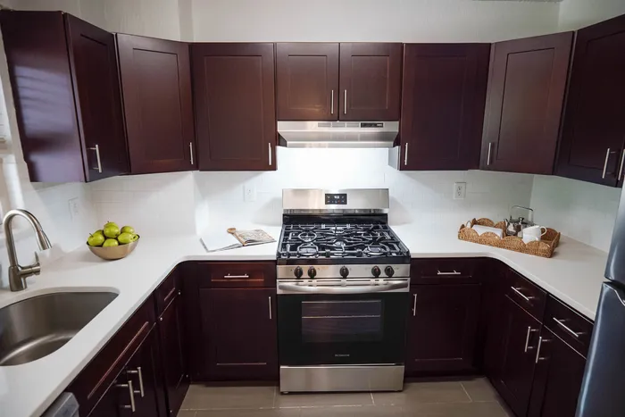 Modern kitchen with sleek dark wood cabinets, stainless steel appliances, and elegant white countertops.