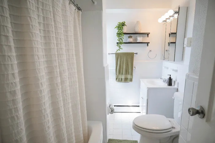 Bright and airy bathroom featuring elegant white tiles, a shower curtain, and stylish shelving with lush greenery accents.