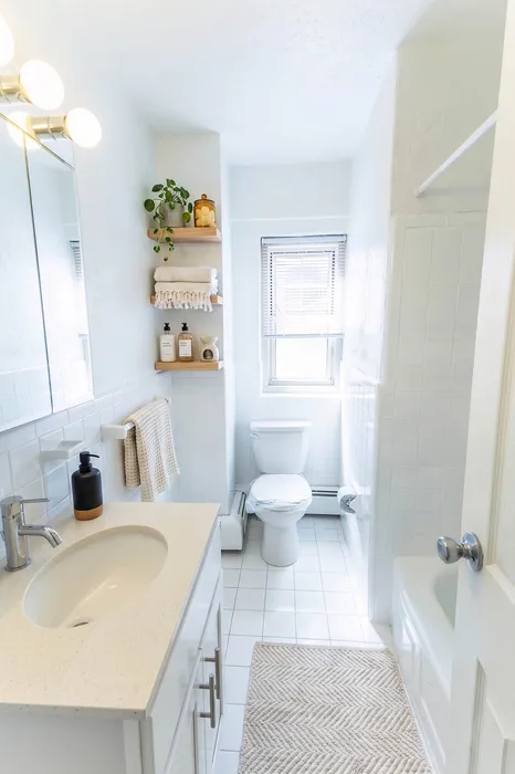 Bright and modern bathroom with elegant white tiles, sleek vanity, and stylish open shelves with plants and toiletries, creating a serene ambiance.