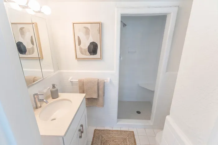 Elegant bathroom design with modern fixtures, featuring a sleek vanity, stylish framed artwork, and a walk-in shower with white tiling.