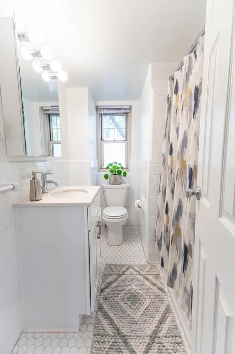 Bright and modern bathroom featuring a stylish vanity, patterned shower curtain, and elegant tile flooring, complete with a sunlit window and vibrant plant accents.