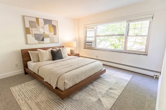 Bright and inviting bedroom featuring a cozy bed with plush pillows, modern abstract artwork, and a large window with a peaceful view.