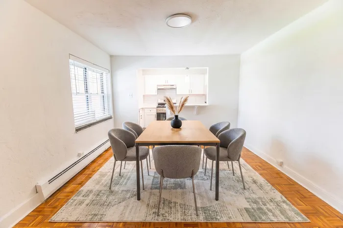 Bright dining area with a modern table and stylish chairs, featuring a cozy kitchen view and natural light from large windows.