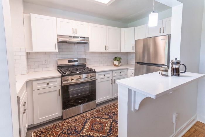 Modern kitchen featuring sleek stainless steel appliances, chic white cabinetry, and elegant white countertops, accented by a stylish backsplash and warm, inviting rug.