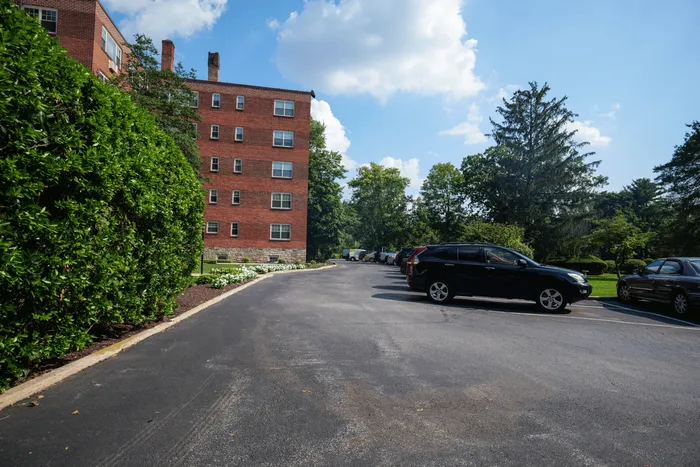 Charming brick apartment building with convenient parking, surrounded by lush greenery and bright blue skies.