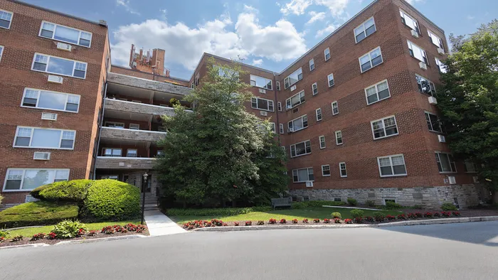 Charming red-brick apartment building with lush landscaping and inviting entrance walkway under a bright blue sky.