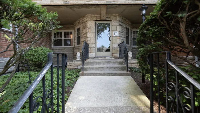 Charming apartment entrance with elegant stone facade, framed by lush greenery and classic wrought-iron railings.