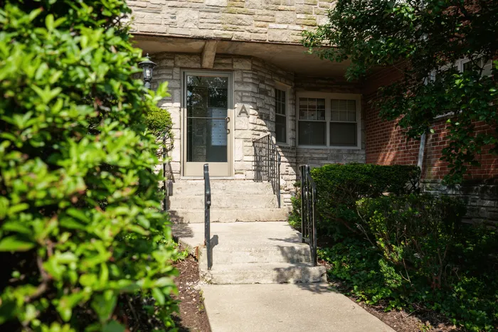 Charming stone entryway with lush greenery leading to a cozy apartment building.