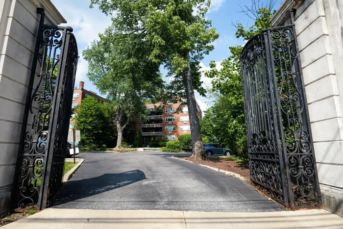 Inviting entrance to a charming apartment complex with elegant wrought iron gates, lush greenery, and a warm, welcoming atmosphere.