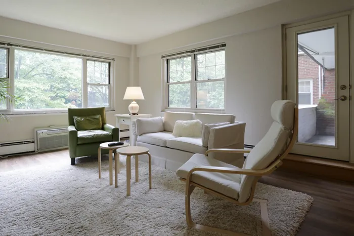 Bright and inviting living room with modern furnishings, large windows offering leafy views, and access to a charming patio.