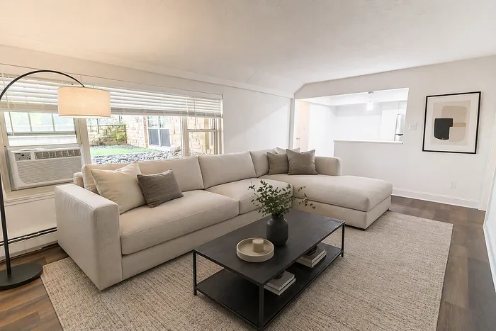 Modern living room with a cozy beige sectional sofa, elegant floor lamp, and a stylish coffee table on a textured rug, offering a bright and inviting ambiance.