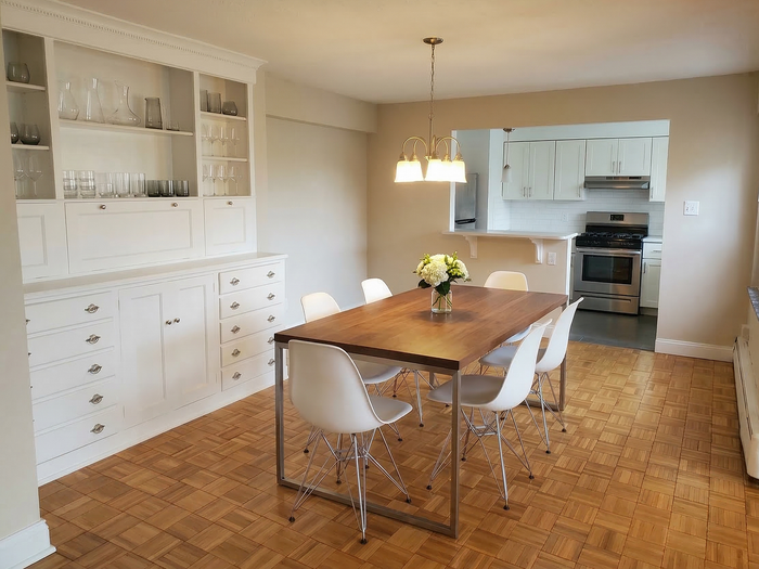 Charming dining room with wooden floor, elegant wooden table, modern white chairs, and a built-in cabinet leading to a sleek kitchen area.