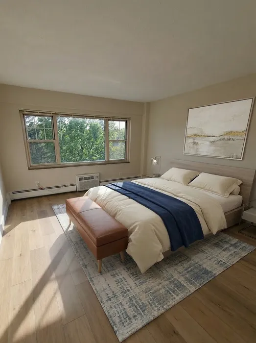 Bright and inviting bedroom with large window, stylish decor, and natural wood flooring.