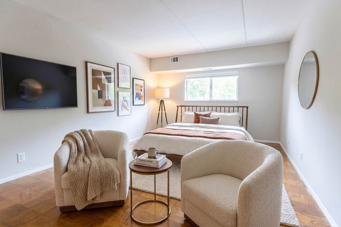 Inviting bedroom with stylish decor, featuring a cozy double bed, elegant armchairs, and modern art on the walls, complemented by natural light from a large window.