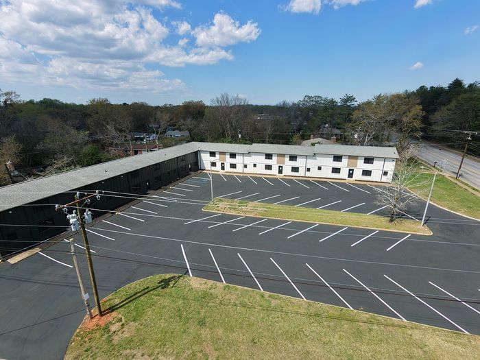 Bright aerial view of a modern apartment complex with spacious parking and lush surroundings, perfect for convenient urban living.