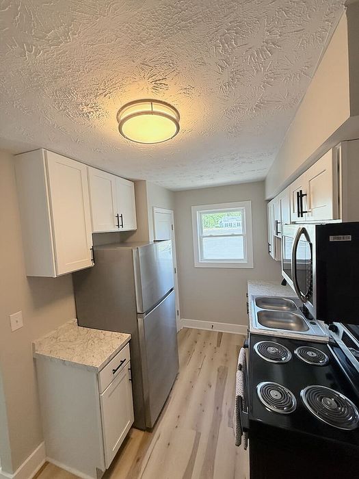 Modern kitchen with sleek stainless steel appliances, elegant cabinetry, and wood-style flooring, illuminated by contemporary lighting.