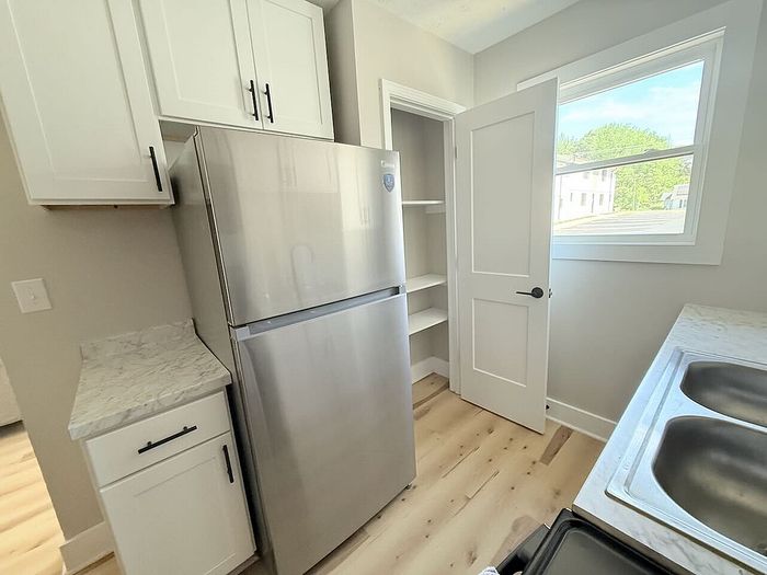 Bright, modern kitchen with sleek stainless steel refrigerator, elegant white cabinetry, and pristine marble countertops.