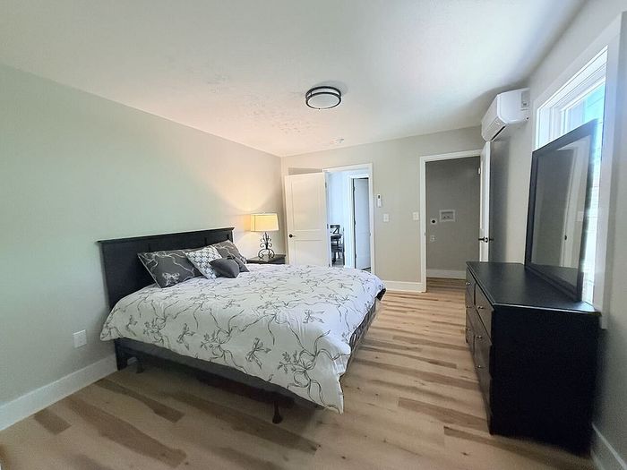 Bright and inviting bedroom with elegant decor, featuring a cozy king-sized bed, stylish nightstand lamp, and natural wood flooring.